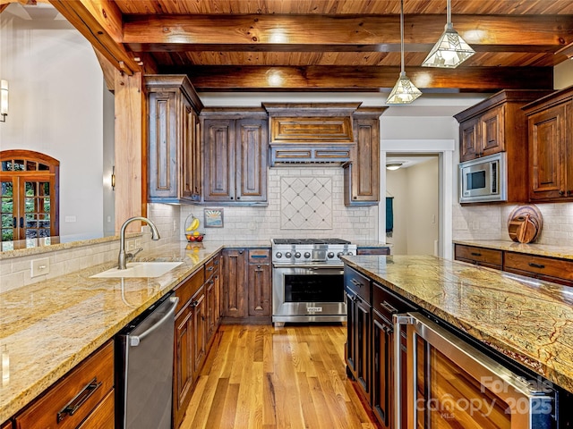 kitchen featuring light wood-style flooring, light stone counters, hanging light fixtures, stainless steel appliances, and a sink