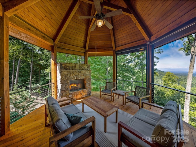 sunroom with vaulted ceiling with beams, a forest view, a stone fireplace, and ceiling fan