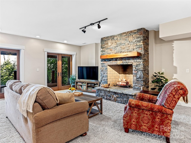 carpeted living area with french doors, a healthy amount of sunlight, a stone fireplace, and track lighting