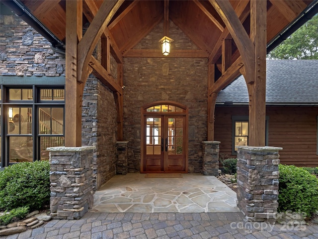 view of exterior entry featuring stone siding, french doors, and a shingled roof