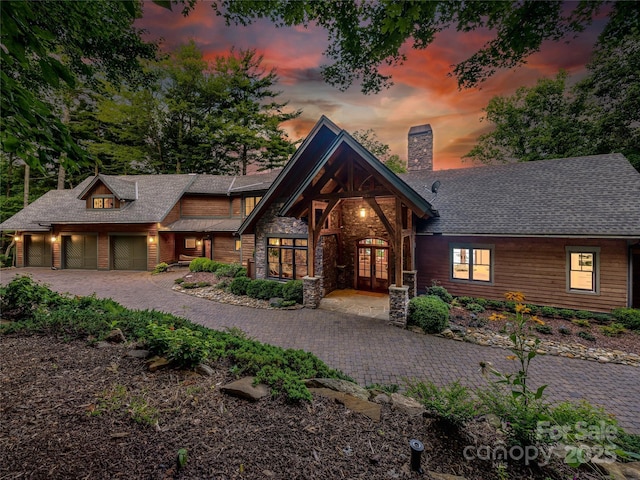 view of front of home with a garage, stone siding, french doors, decorative driveway, and a chimney