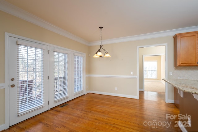 unfurnished dining area featuring ornamental molding, a chandelier, and light wood-type flooring