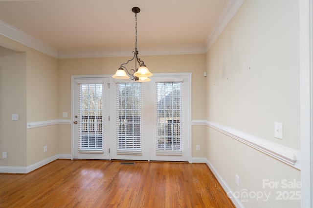 unfurnished dining area featuring an inviting chandelier, crown molding, and hardwood / wood-style floors