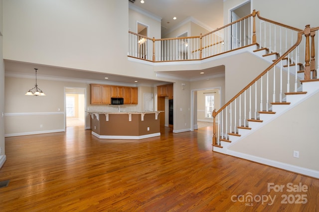 unfurnished living room with hardwood / wood-style flooring, a towering ceiling, ornamental molding, and an inviting chandelier