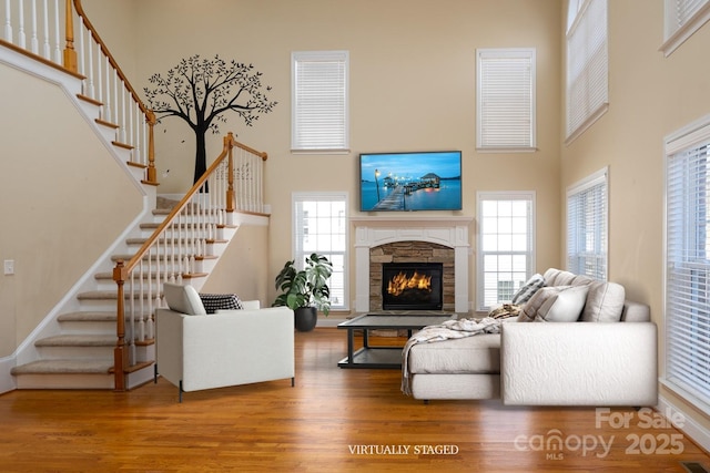 living room with a towering ceiling, a healthy amount of sunlight, a fireplace, and hardwood / wood-style floors