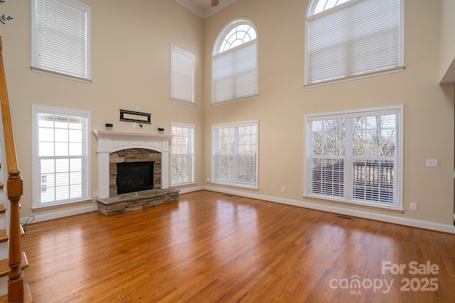 unfurnished living room featuring hardwood / wood-style flooring, a stone fireplace, and a high ceiling