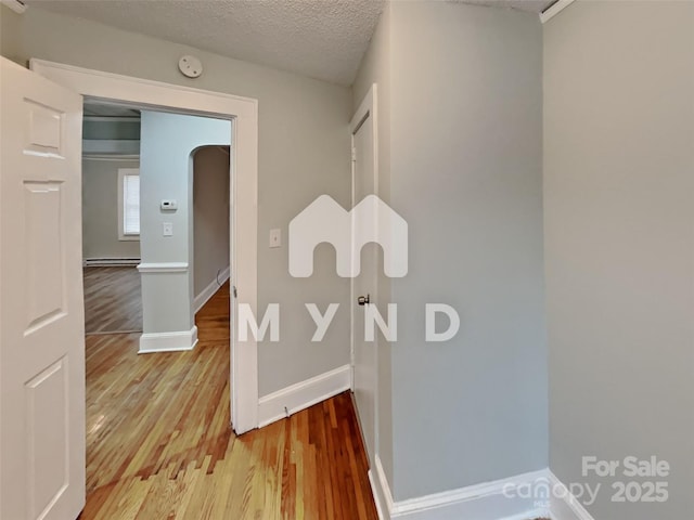 hall with a baseboard heating unit, wood-type flooring, and a textured ceiling