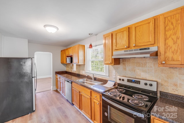 kitchen featuring under cabinet range hood, a sink, backsplash, dark countertops, and appliances with stainless steel finishes