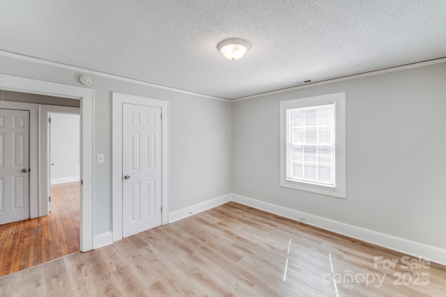 empty room featuring a textured ceiling, wood finished floors, visible vents, and baseboards