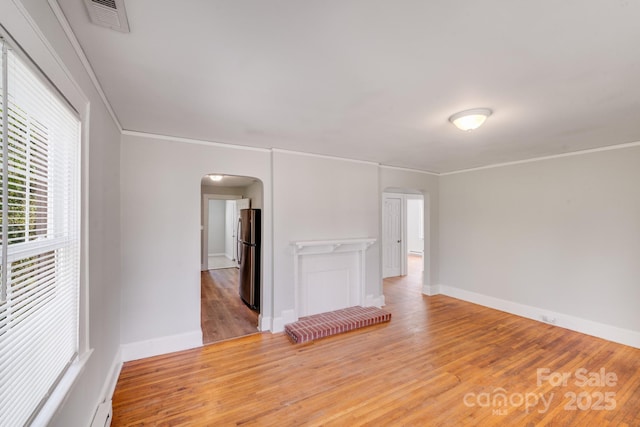 empty room with visible vents, crown molding, baseboards, wood finished floors, and arched walkways