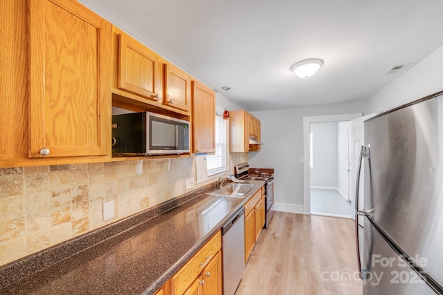 kitchen featuring a sink, tasteful backsplash, light wood-style floors, appliances with stainless steel finishes, and baseboards