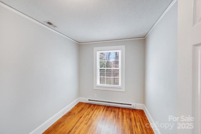 spare room featuring visible vents, a textured ceiling, crown molding, light wood-type flooring, and baseboard heating