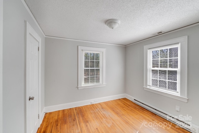 empty room with visible vents, ornamental molding, light wood-style floors, a baseboard radiator, and baseboards