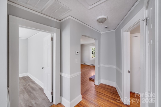 hallway featuring attic access, arched walkways, light wood finished floors, and ornamental molding