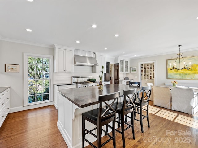 kitchen featuring a kitchen island, a breakfast bar, white cabinets, stove, and wall chimney range hood