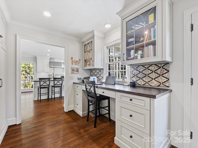 home office with crown molding, built in desk, and dark hardwood / wood-style floors