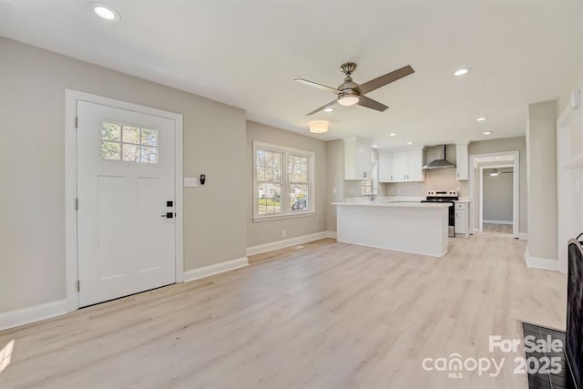 interior space featuring ceiling fan, electric range, white cabinets, kitchen peninsula, and wall chimney exhaust hood