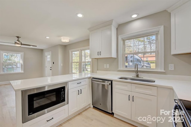 kitchen featuring stainless steel appliances, sink, white cabinetry, kitchen peninsula, and a healthy amount of sunlight