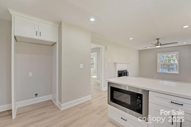 kitchen featuring built in microwave, white cabinetry, ceiling fan, and light wood-type flooring