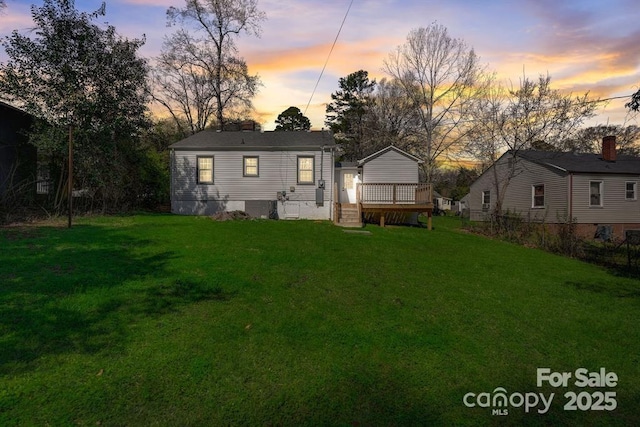 back house at dusk with a wooden deck and a yard