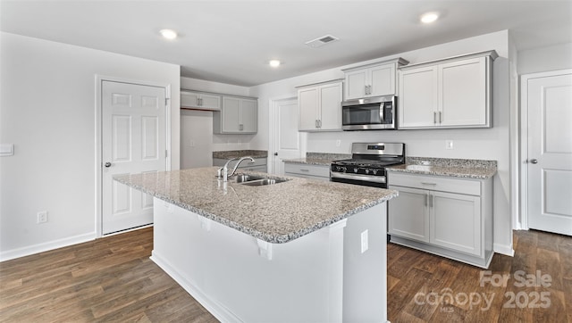 kitchen featuring an island with sink, appliances with stainless steel finishes, sink, and light stone counters