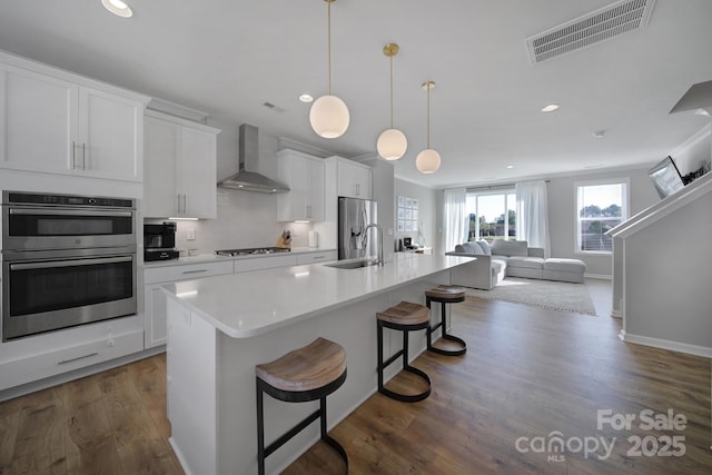 kitchen featuring appliances with stainless steel finishes, an island with sink, sink, a breakfast bar area, and wall chimney range hood