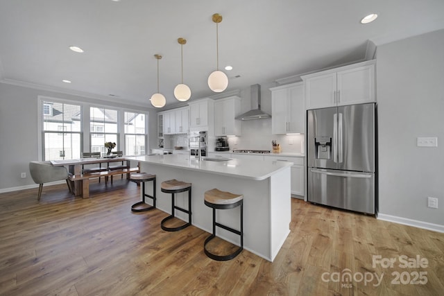 kitchen with wall chimney exhaust hood, a center island with sink, appliances with stainless steel finishes, a kitchen breakfast bar, and white cabinets