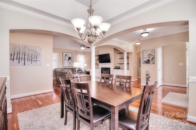 dining area featuring built in features, decorative columns, ornamental molding, light hardwood / wood-style floors, and ceiling fan with notable chandelier