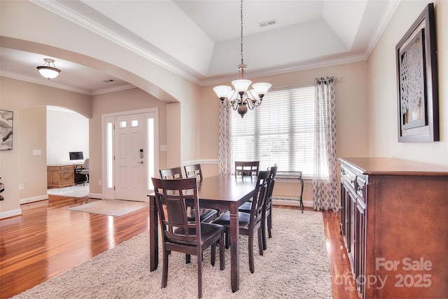 dining area featuring an inviting chandelier, ornamental molding, a raised ceiling, and light wood-type flooring