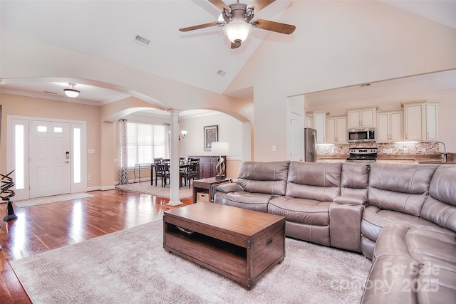 living room featuring ornate columns, high vaulted ceiling, sink, crown molding, and light hardwood / wood-style flooring