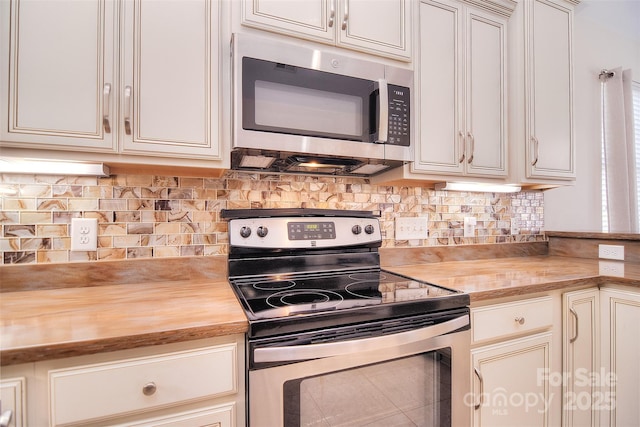 kitchen with appliances with stainless steel finishes, butcher block counters, cream cabinets, and backsplash