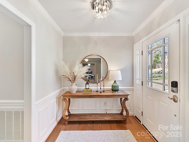 foyer entrance featuring hardwood / wood-style flooring, crown molding, and a notable chandelier