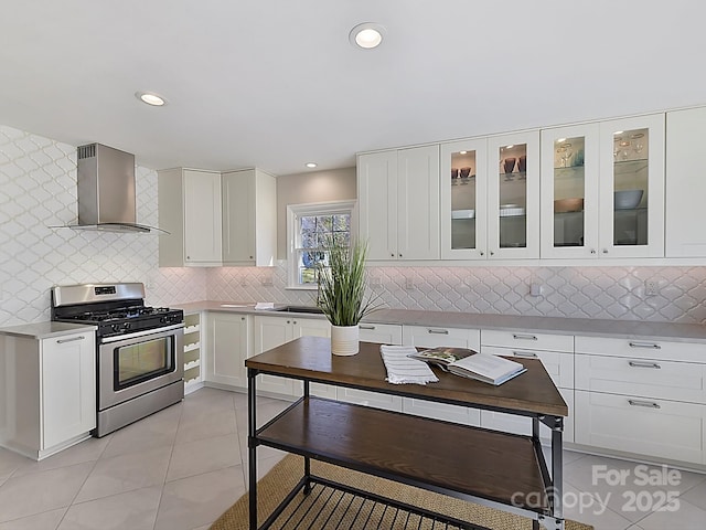 kitchen featuring light tile patterned flooring, wall chimney exhaust hood, stainless steel gas range oven, white cabinetry, and tasteful backsplash