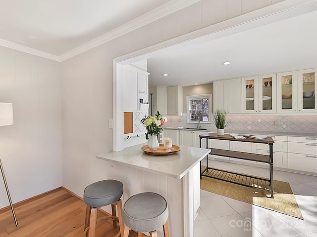 kitchen featuring sink, white cabinetry, tasteful backsplash, ornamental molding, and a kitchen breakfast bar