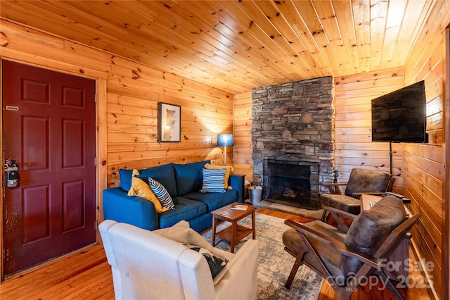 living room featuring wood ceiling, wooden walls, a fireplace, and light wood-type flooring