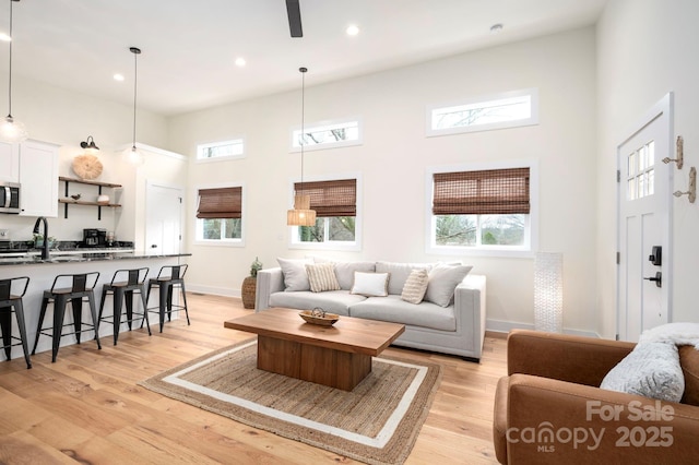 living room featuring sink, a towering ceiling, a wealth of natural light, and light wood-type flooring