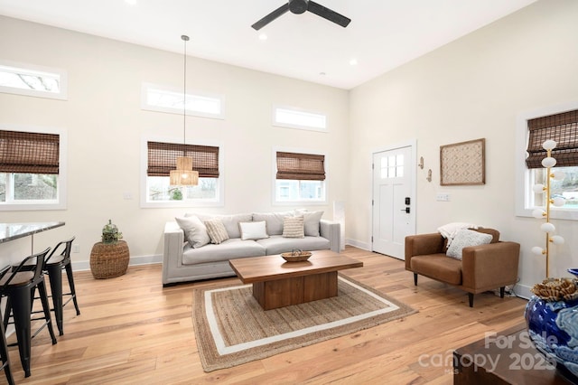 living room featuring ceiling fan, a high ceiling, and light wood-type flooring