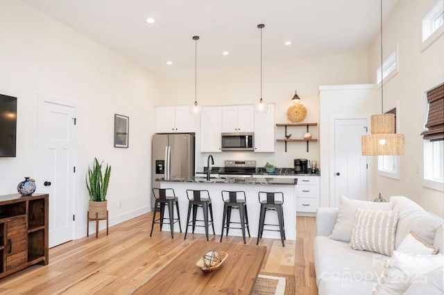 kitchen featuring a breakfast bar, white cabinetry, hanging light fixtures, a kitchen island with sink, and stainless steel appliances
