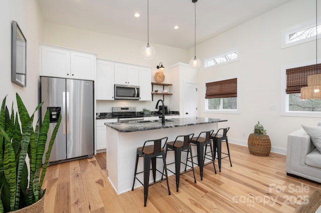 kitchen with appliances with stainless steel finishes, white cabinetry, sink, a kitchen bar, and a kitchen island with sink