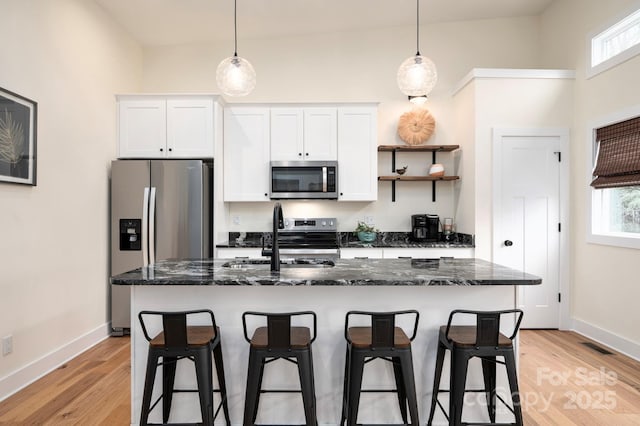 kitchen with appliances with stainless steel finishes, white cabinetry, sink, dark stone countertops, and a kitchen island with sink