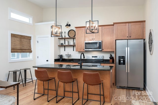 kitchen with appliances with stainless steel finishes, pendant lighting, an island with sink, sink, and light wood-type flooring