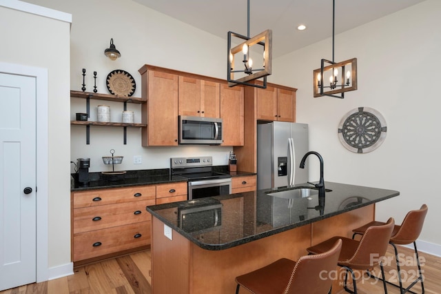 kitchen featuring sink, light hardwood / wood-style flooring, appliances with stainless steel finishes, hanging light fixtures, and a center island with sink