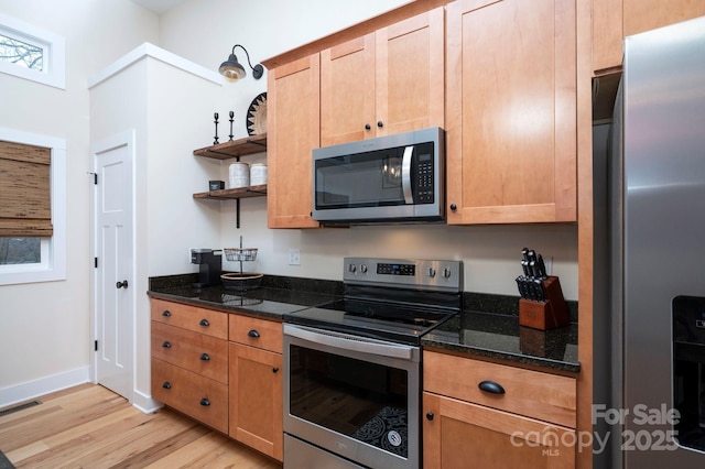 kitchen featuring appliances with stainless steel finishes, light wood-type flooring, and dark stone counters