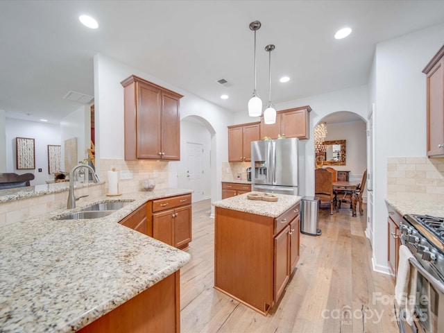 kitchen with sink, stainless steel appliances, a center island, light stone countertops, and decorative light fixtures