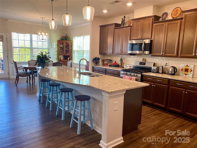 kitchen featuring sink, a breakfast bar area, hanging light fixtures, appliances with stainless steel finishes, and a kitchen island with sink