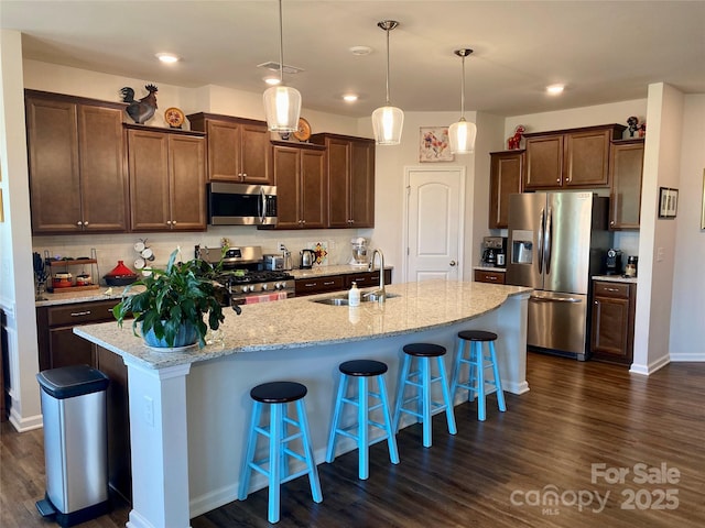 kitchen featuring sink, hanging light fixtures, stainless steel appliances, a kitchen breakfast bar, and an island with sink