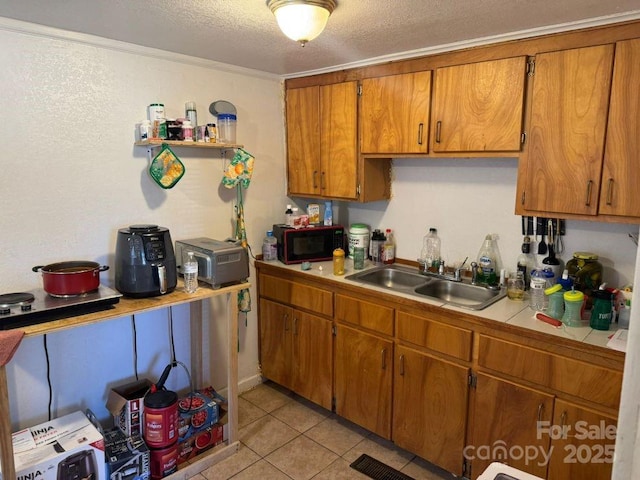 kitchen with light tile patterned flooring, sink, tile counters, crown molding, and a textured ceiling