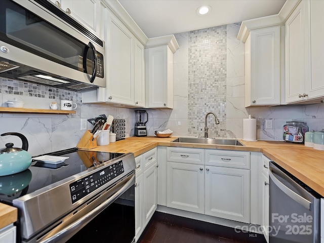 kitchen with appliances with stainless steel finishes, butcher block counters, sink, and white cabinets