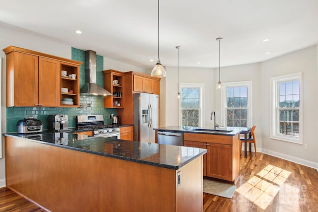 kitchen featuring sink, dark stone counters, hanging light fixtures, stainless steel appliances, and wall chimney exhaust hood