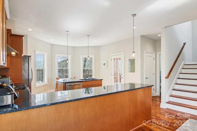 kitchen featuring sink, dark stone countertops, stainless steel appliances, a center island, and decorative light fixtures